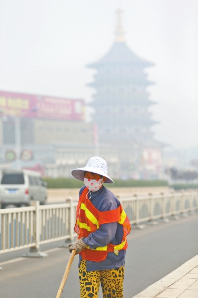 近日，在古都洛陽(yáng)，環(huán)衛(wèi)工人身后的“天堂”被霧霾籠罩著。