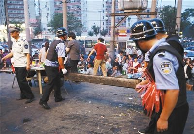 6月13日晚8點，朝陽路和青年路交叉口西側(cè)，一次聯(lián)合執(zhí)法行動中，輔警與協(xié)管抬走商戶的燒烤用具。新京報記者 尹亞飛 攝