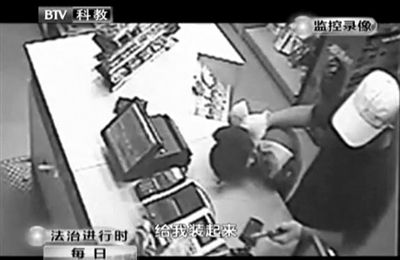 戴帽男子一手掐住加油站營業(yè)員，一手持發(fā)令槍指向另一營業(yè)員，要求“把錢給我裝起來”。