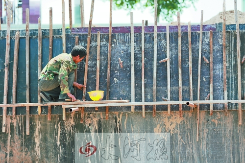 　　烈日下，狹窄的架子上，工人正用錘子固定樁基。