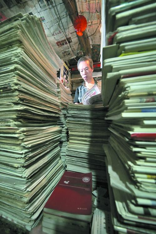 王曉民坐在寫字桌前，被報紙淹沒。