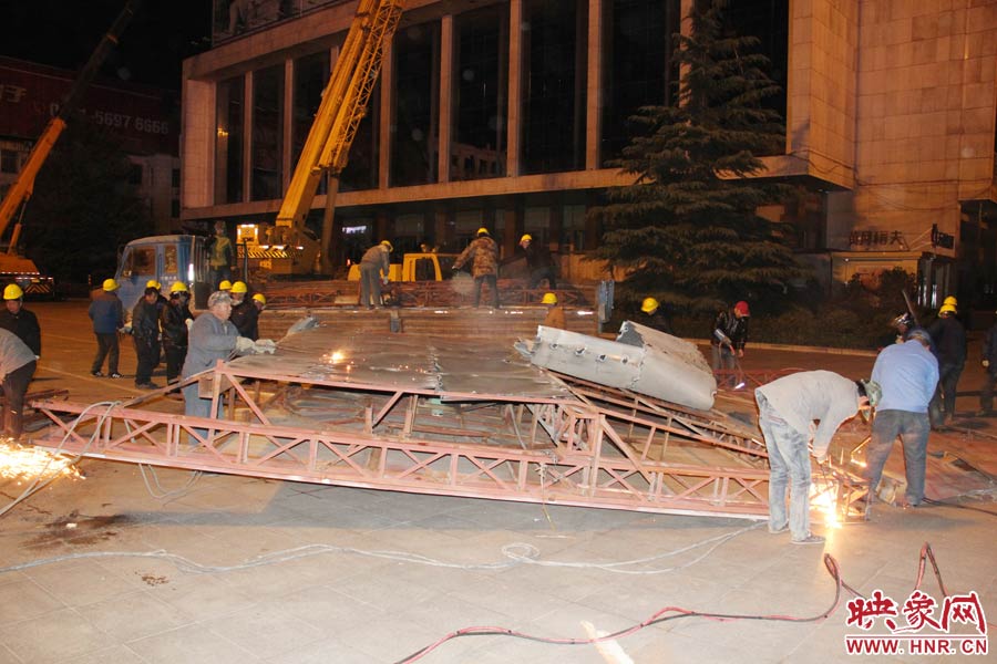 地面上的20多名工人對吊裝下的廣告牌進行分割。