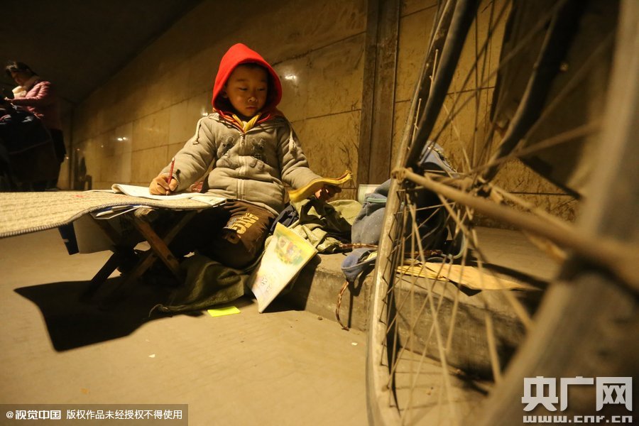 2015年11月8日晚，鄭州，7歲男孩涵洞橋下陪父母練攤，路邊燈下坐小馬扎上寫作業(yè)。