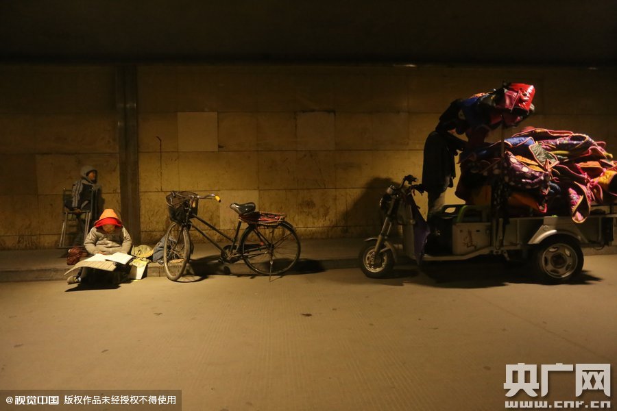 2015年11月8日晚，鄭州，7歲男孩涵洞橋下陪父母練攤，路邊燈下坐小馬扎上寫作業(yè)。