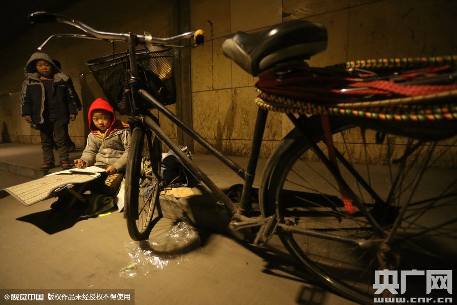 2015年11月8日晚，鄭州，7歲男孩涵洞橋下陪父母練攤，路邊燈下坐小馬扎上寫作業(yè)。
