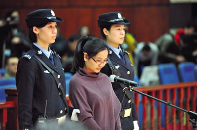 被告人盧梅低著頭，站在朝陽法院刑事審判庭的被告席上。