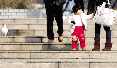 昨天中午，一女孩拉著家長(zhǎng)的手在紫荊山公園曬太陽(yáng)，氣溫升高，孩子的棉衣解開(kāi)了扣子。