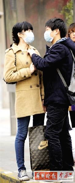 公交站臺上，一對年輕人戴著口罩，系緊衣領(lǐng)。